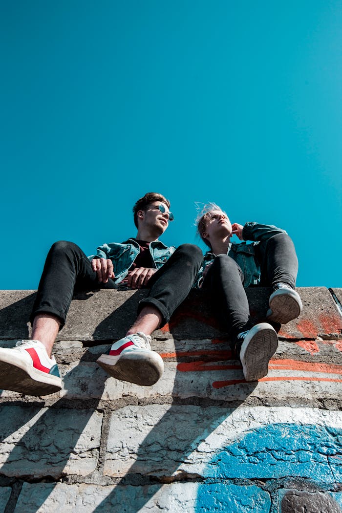 Services-02 Two young people sitting on a stone wall under a vibrant blue sky, enjoying a sunny day together.