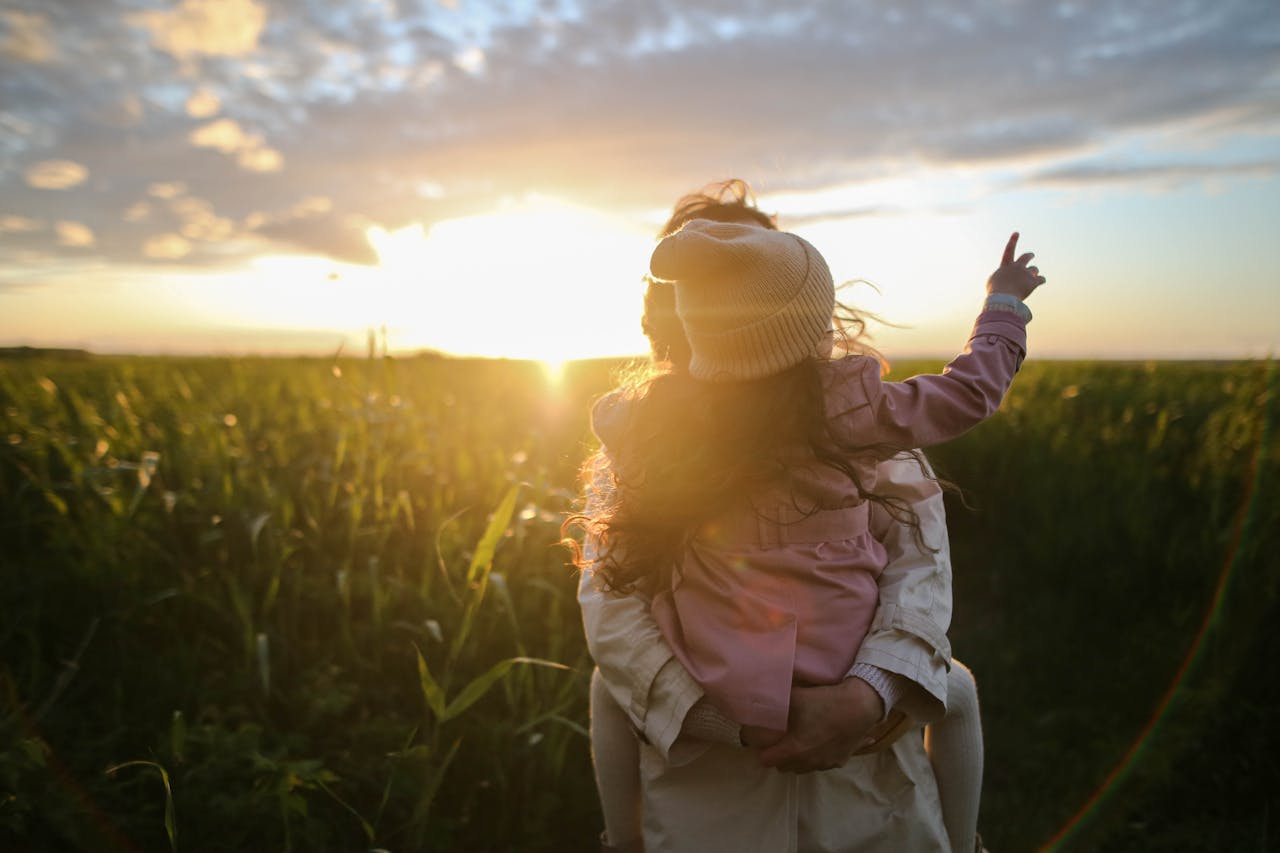creative-02 A mother and daughter embrace and point at the sunset in a grassy field.